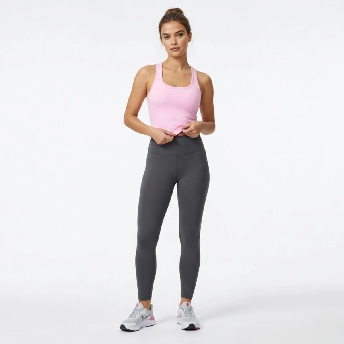 Full body view of model adjusting the Kouvr pink luxury athleisure crop top with dark grey leggings and sneakers