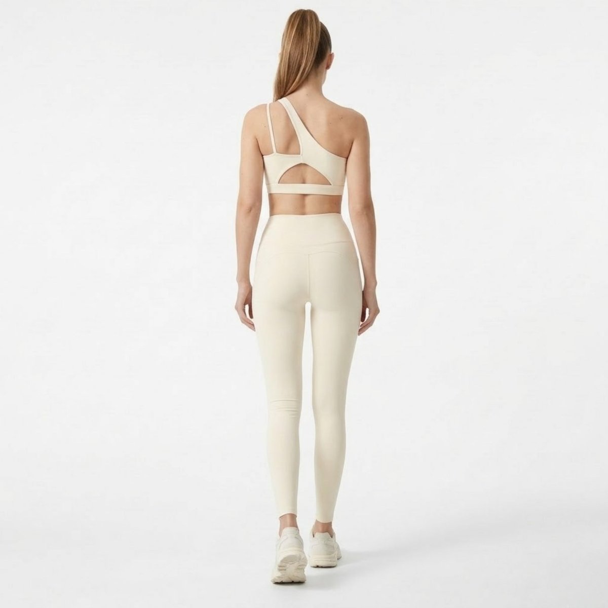 Back view of Kouvr apricot workout set showing the architectural back cutout detail on the asymmetrical sports bra and curved glute seams.