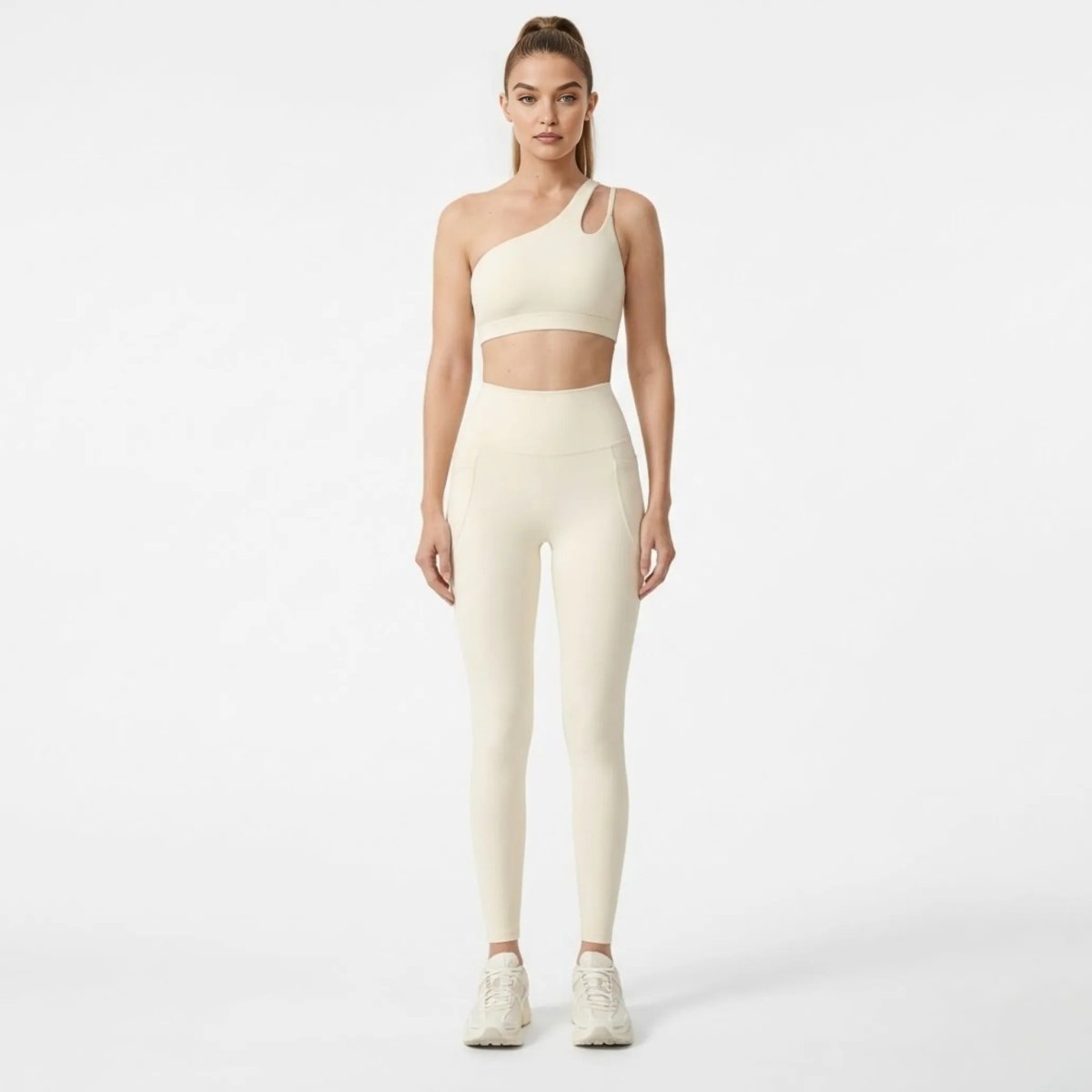 Front view of female model wearing Kouvr luxury apricot one shoulder sports bra with cutouts and matching high waisted activewear leggings.