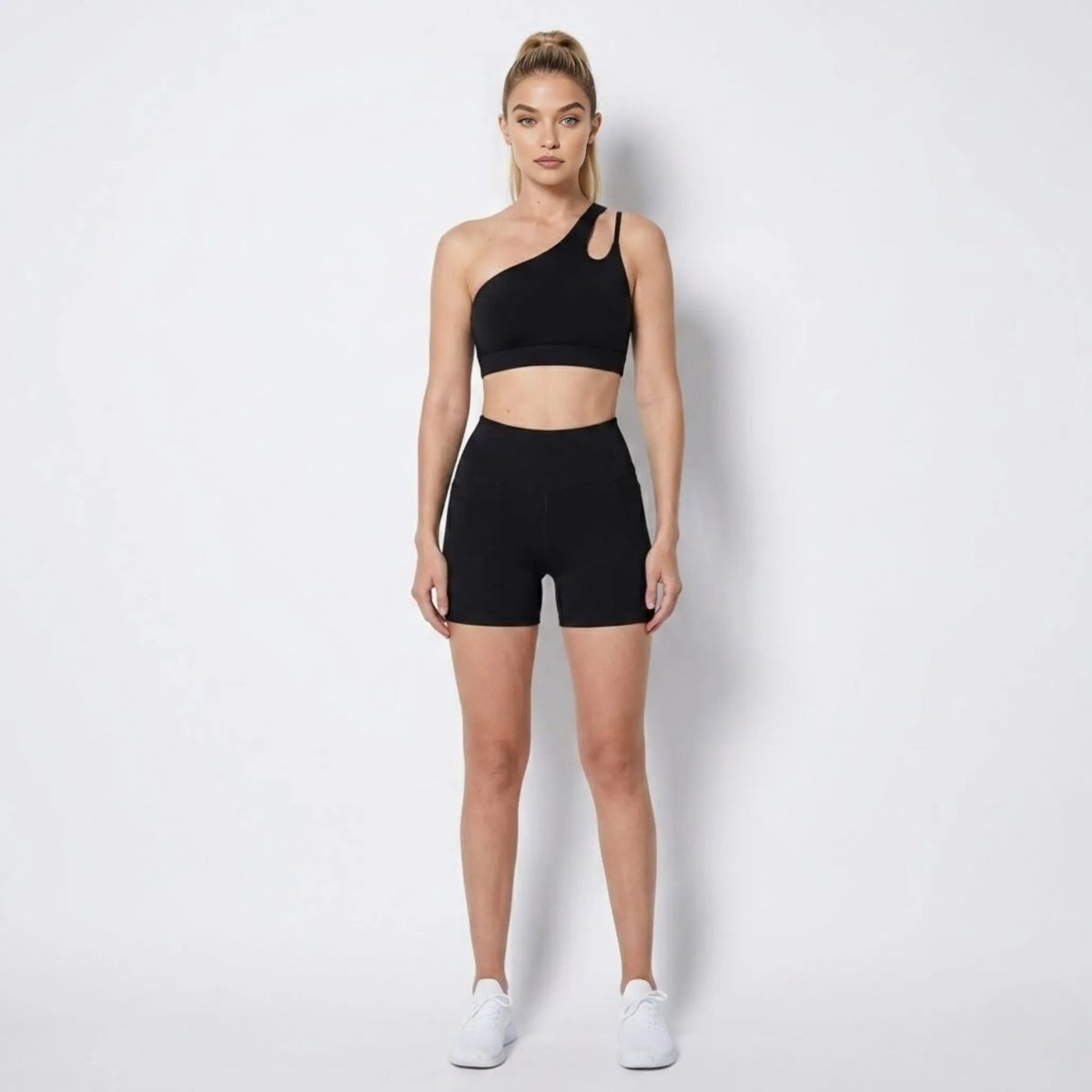 Woman wearing Kouvr black asymmetrical one shoulder activewear set with high waisted biker shorts facing forward