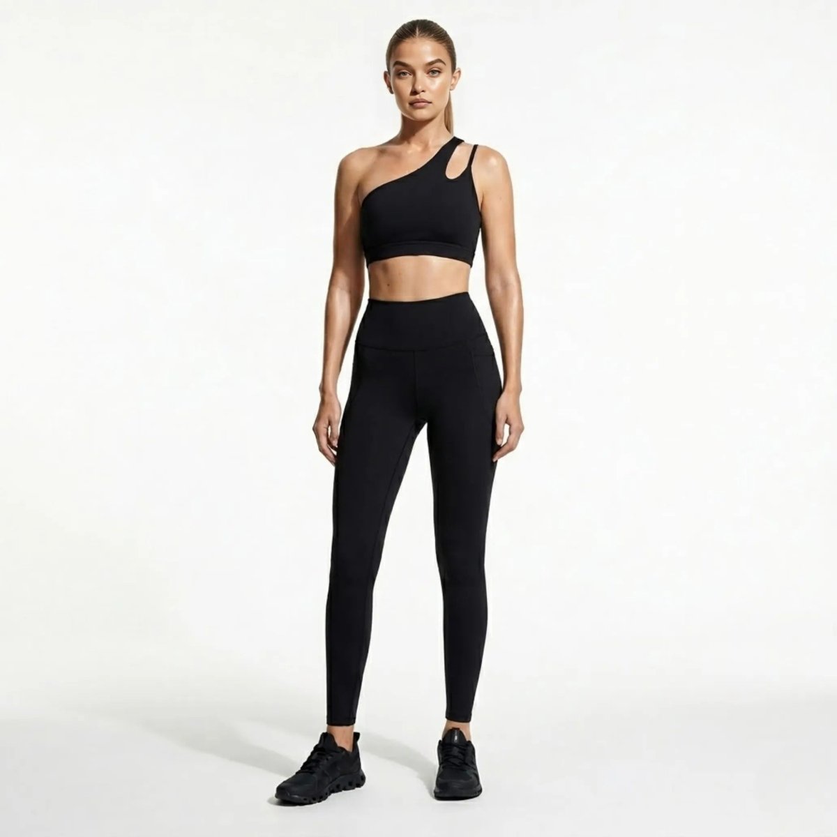 Woman wearing Kouvr black asymmetrical one shoulder sports bra and high waisted leggings with pockets front view