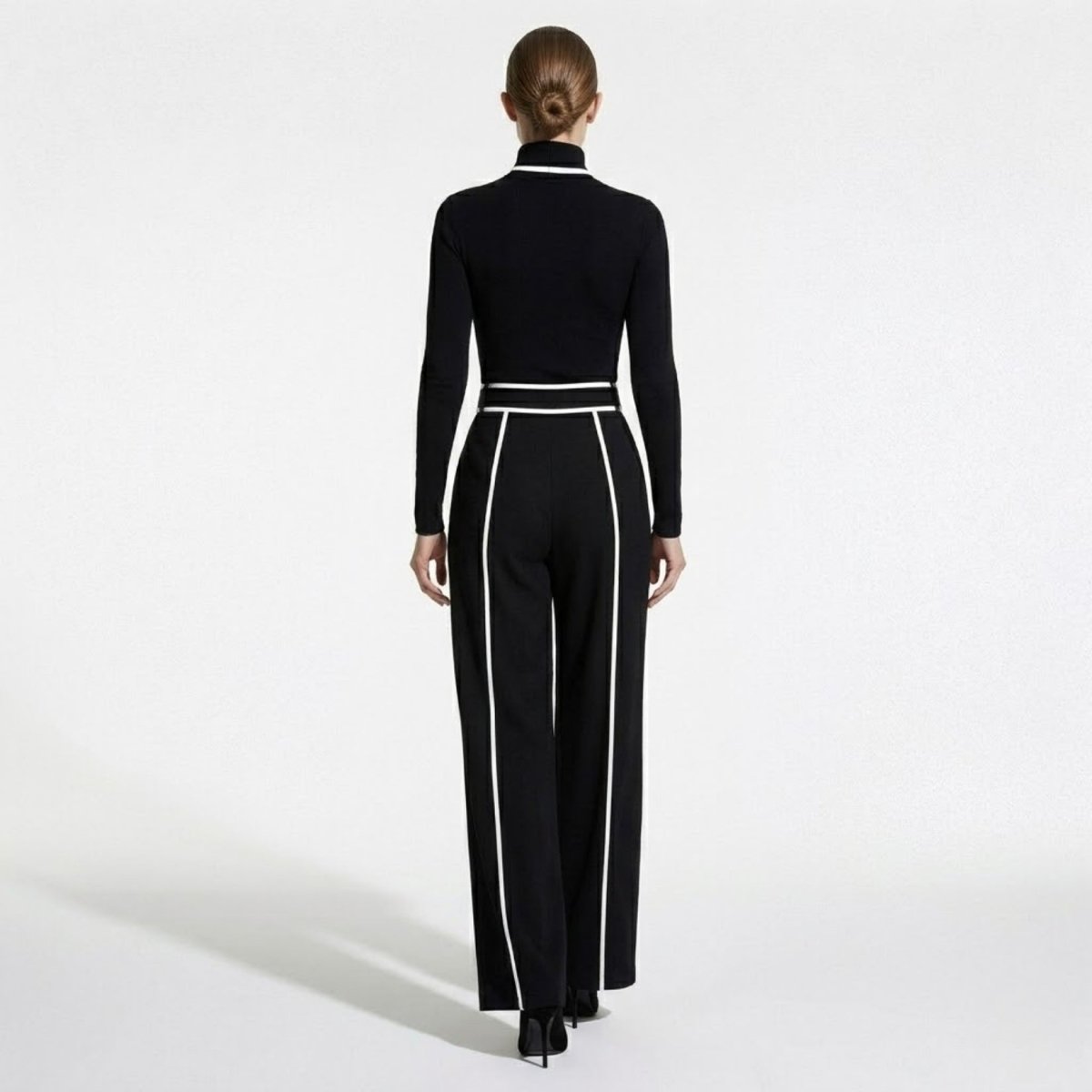 Back view of woman modeling black and white piped wide leg designer jumpsuit with form-fitting bodice.
