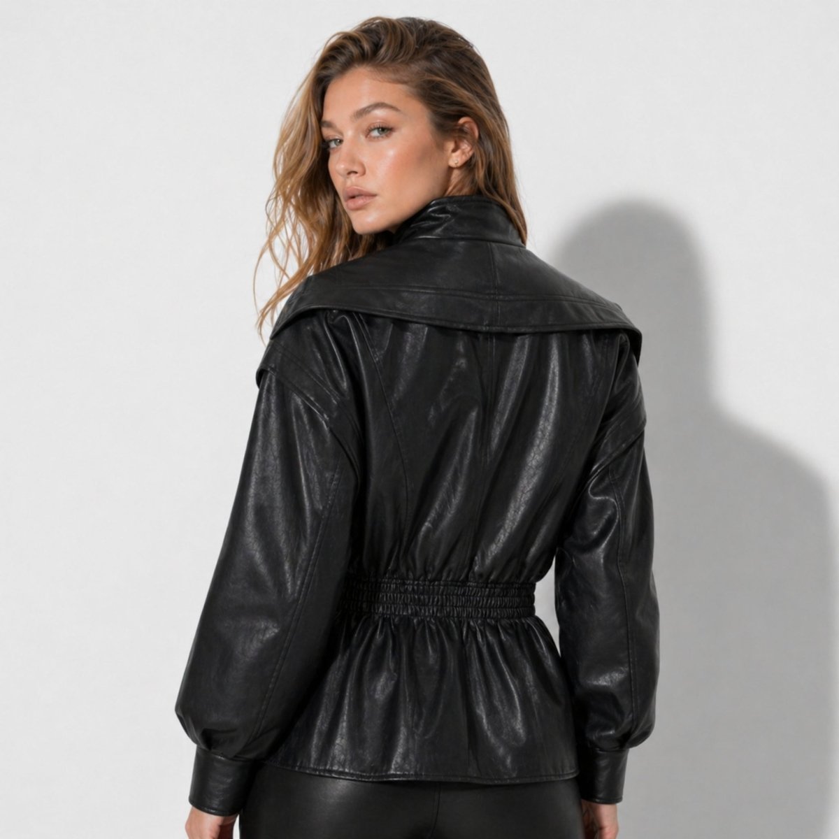 Back view of women's black faux leather jacket showing shirred elastic waist and draped collar styling by Kouvr.