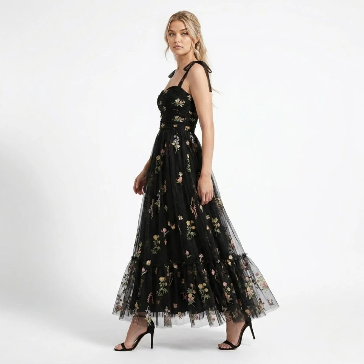 Side profile of woman walking in Kouvr black floral embroidered tulle maxi gown showing tiered skirt and botanical details.