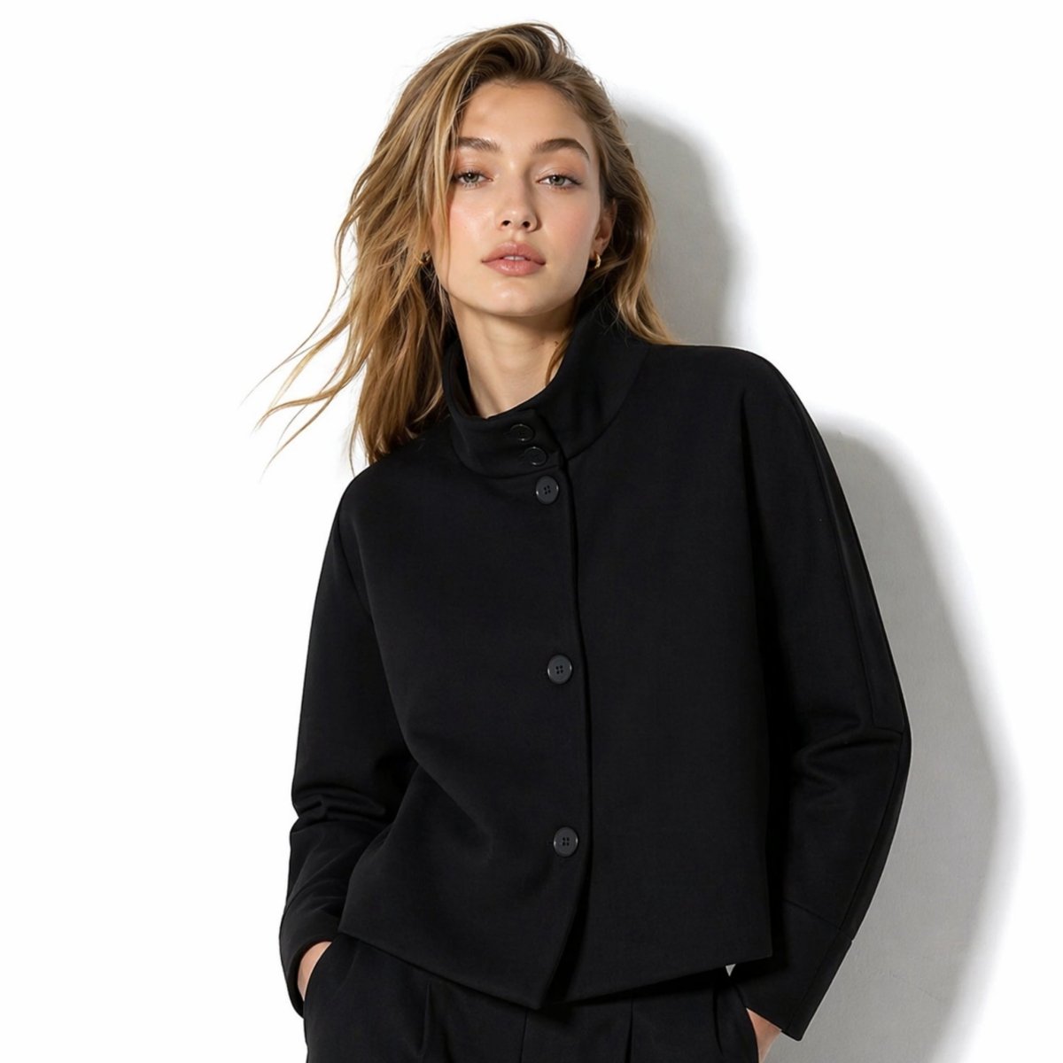 Woman wearing Kouvr black funnel neck structured cropped jacket with asymmetrical buttons.