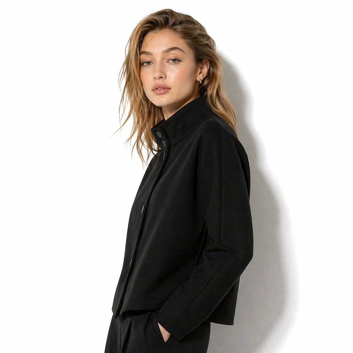 Side profile of the minimalist black mock neck boxy jacket by Kouvr styled with matching black trousers.