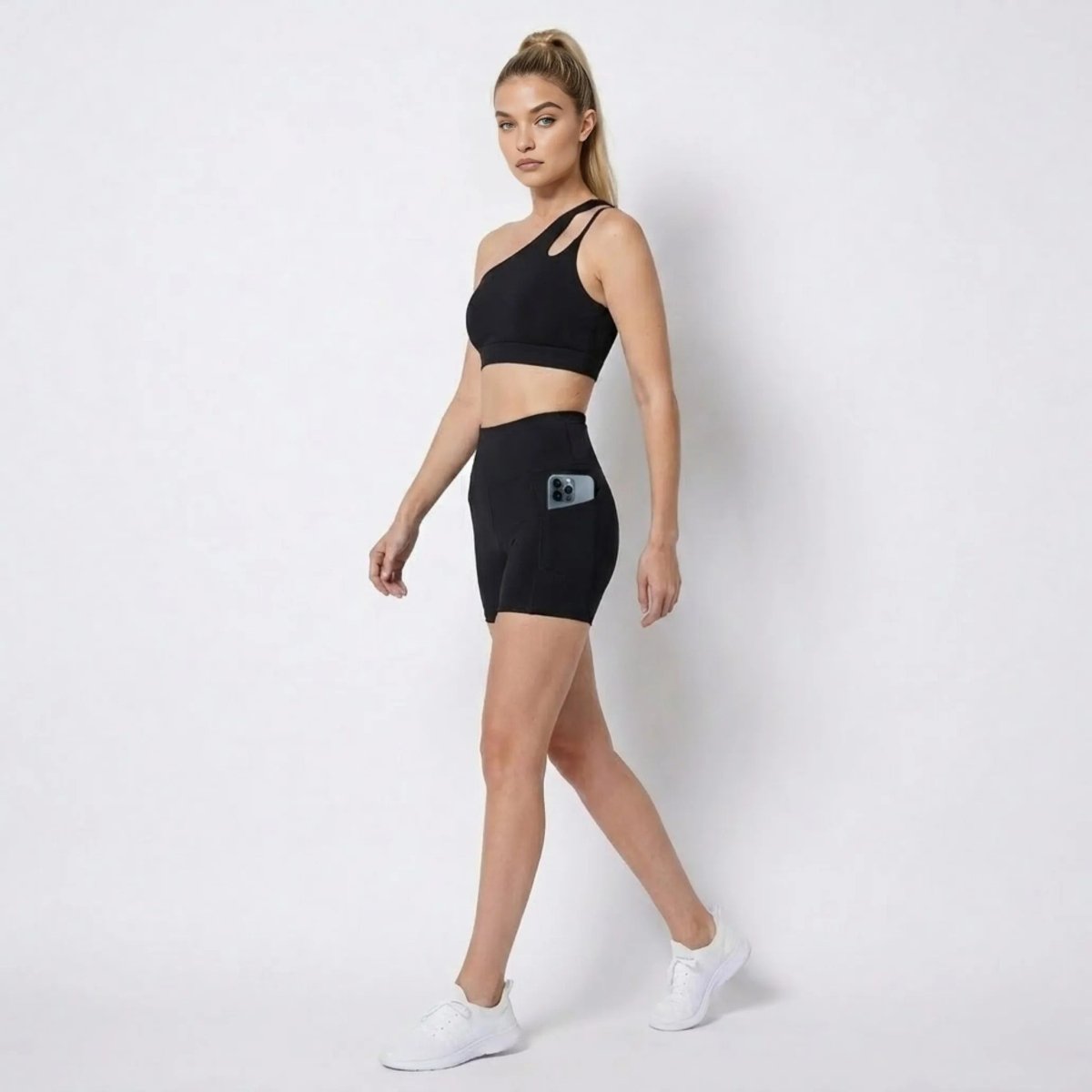 Side profile of woman walking in Kouvr black high waisted biker shorts showing functional side phone pocket