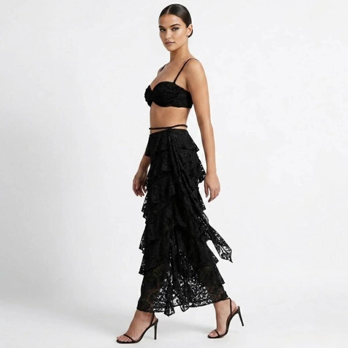Side profile of woman modeling a black sheer lace asymmetrical tiered maxi skirt and ruched crop top