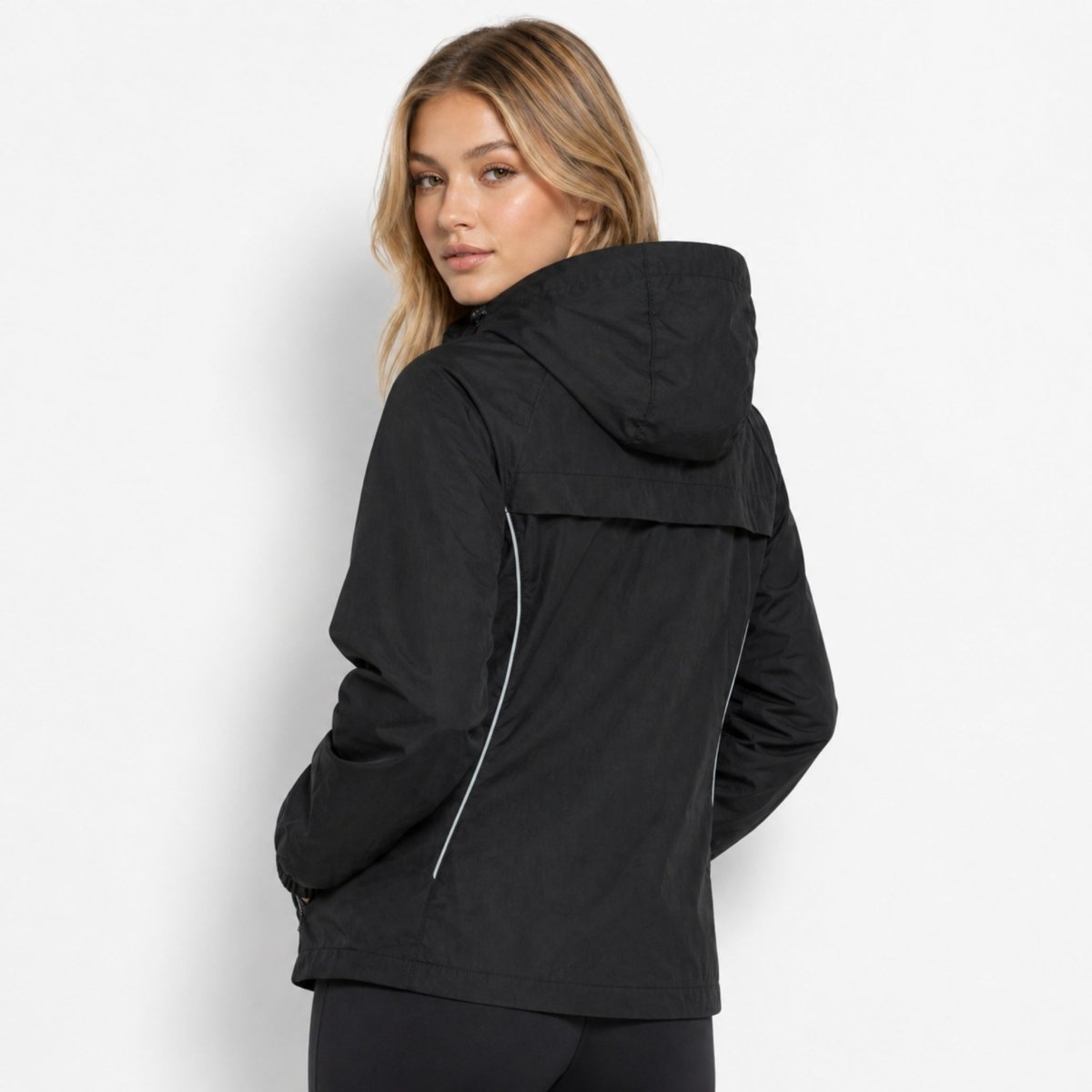 Back view of woman in Kouvr black activewear jacket highlighting breathable back vent flap and reflective piping.