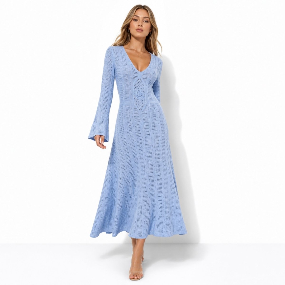 Woman wearing a luxury light blue crochet long sleeve maxi dress with v-neck and bell sleeves walking forward against a white background.