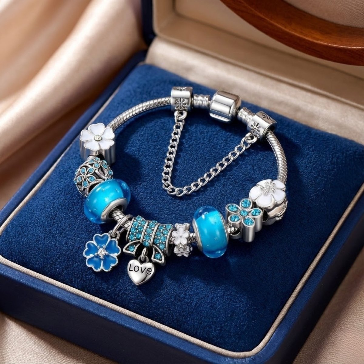 Silver charm bracelet featuring blue Murano glass beads, blue floral charms, and a dangling "Love" heart charm isolated on a white background.