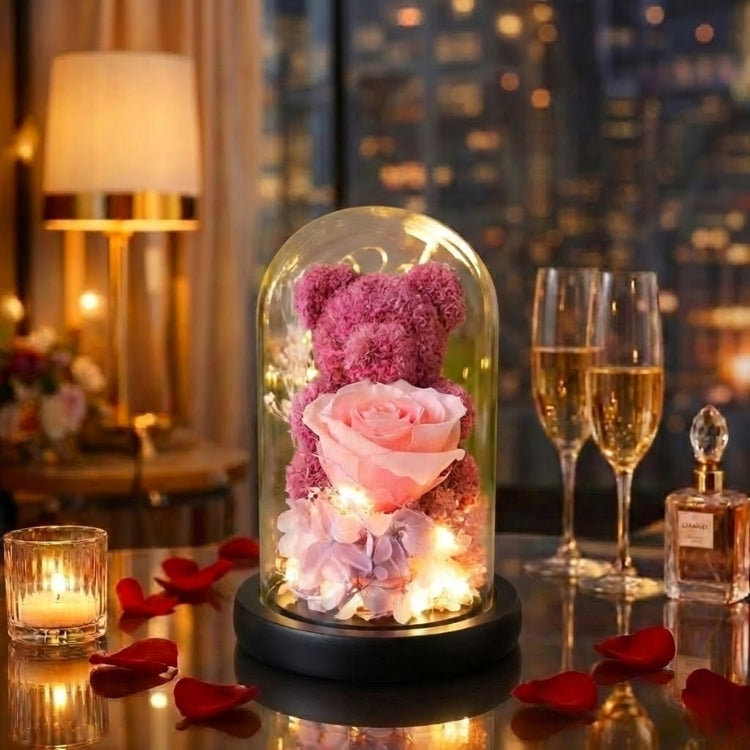 Elegant blush pink moss bear holding a preserved rose in a glowing glass dome with a natural wood base.