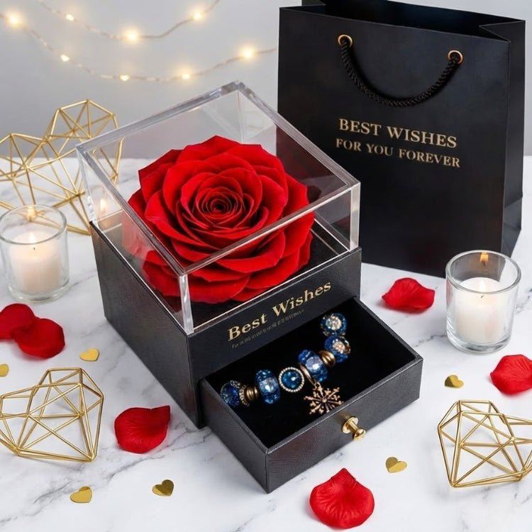 A classic large red eternal rose in a black display box with a clear lid, set on a marble table with rose petals.