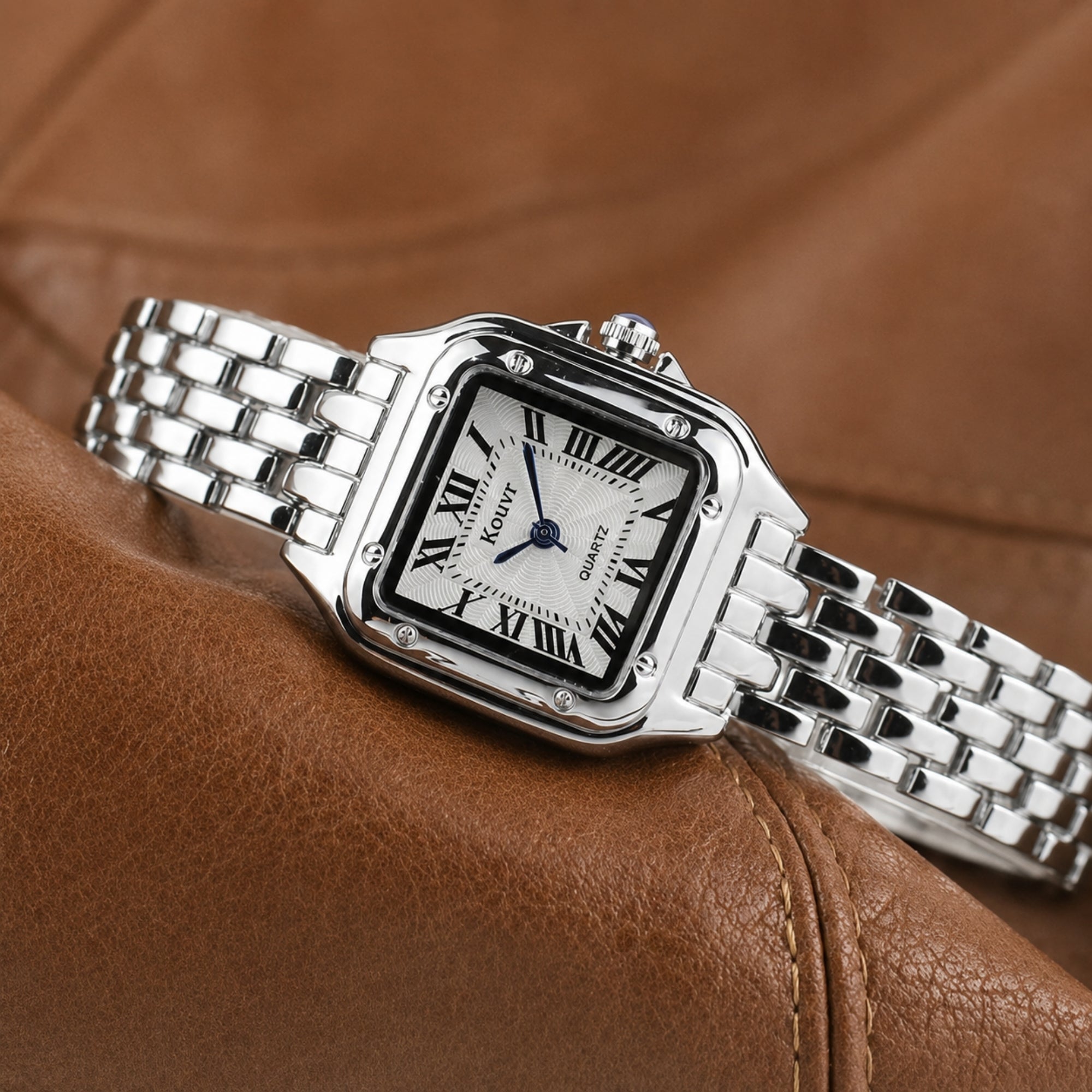 Kouvr silver polished stainless steel women's dress watch with square dial resting on a rich brown textured leather background.
