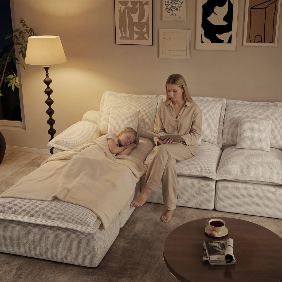 A woman reading a book to a child sleeping on a cozy, oversized beige pit sofa under warm lamp lighting.