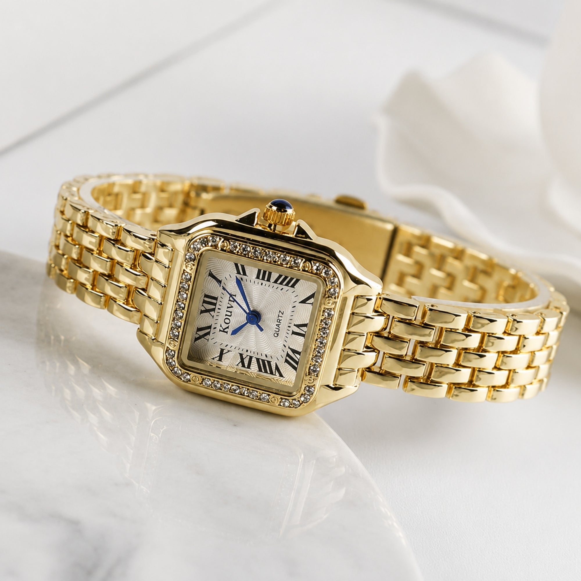 Angled view of the Kouvr women's gold square watch with crystal bezel resting on a luxury white marble surface.
