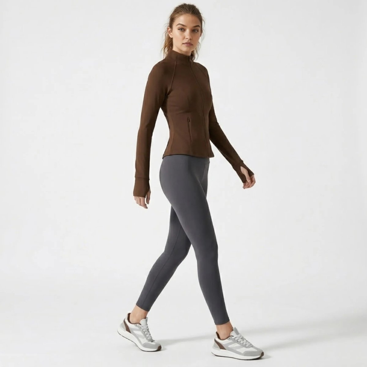 Female model walking wearing the Kouvr tailored brown workout jacket showcasing four-way stretch