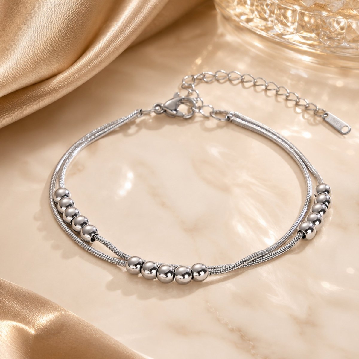 Close up of elegant S925 silver double layered beaded ankle bracelet on smooth beige silk.