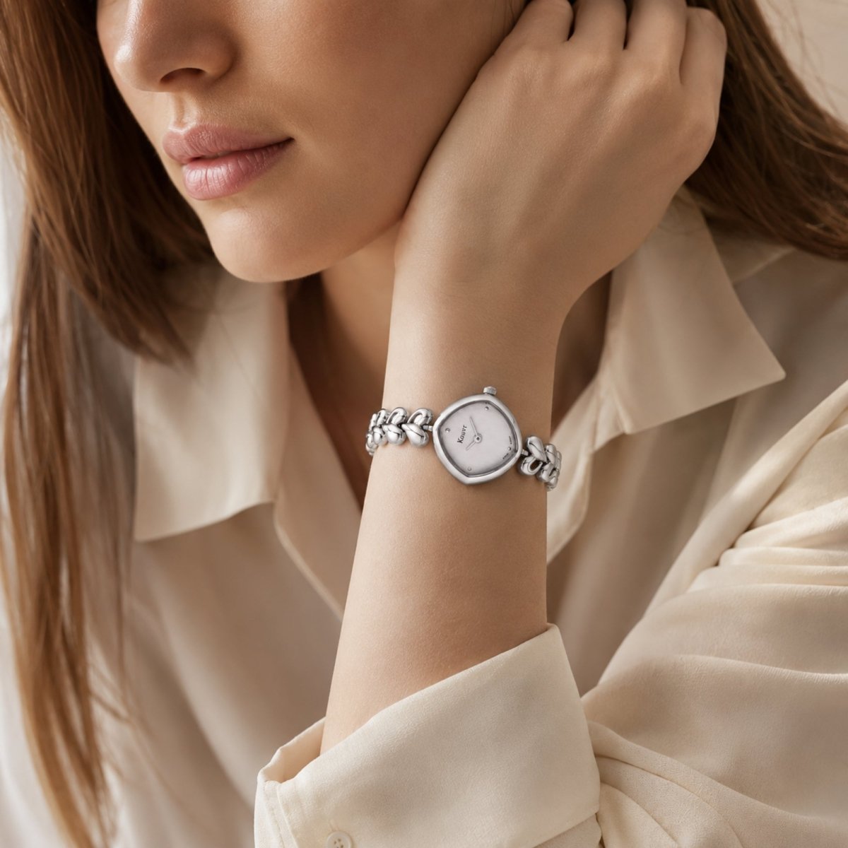 Close up lifestyle shot of a woman's wrist wearing the delicate Kouvr silver vintage style watch paired with a soft beige silk shirt.
