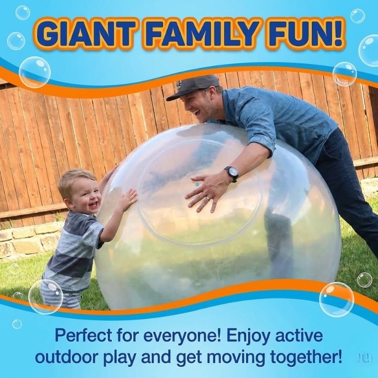 A father and his toddler son laughing while pushing a giant clear bubble ball together in the backyard.