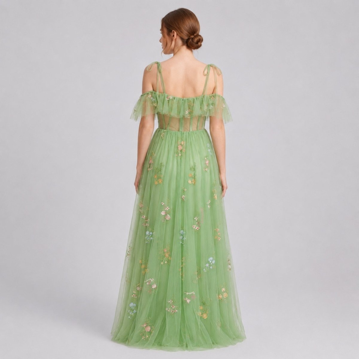 Back view of model in green floral tulle maxi dress highlighting delicate tie-shoulder straps and sheer corset back detailing.