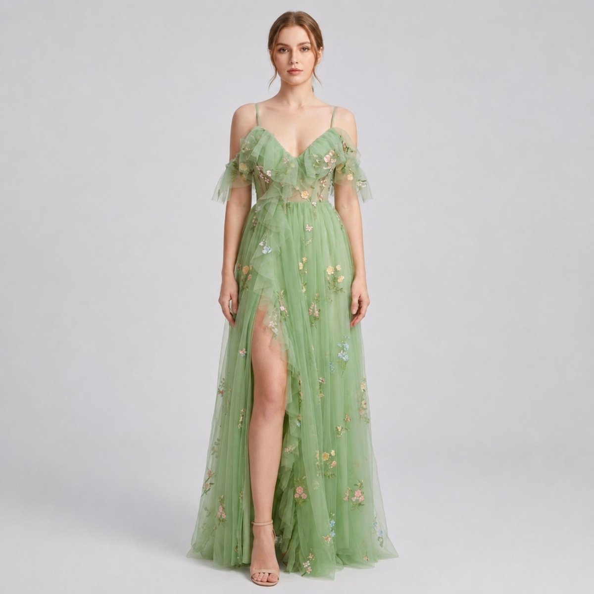 Elegant woman wearing a green floral embroidered tulle maxi dress with corset bodice and high leg slit, front full body view.
