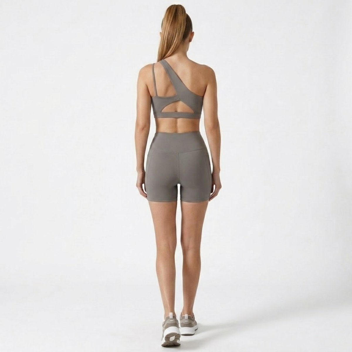 Back view highlighting the cutout strap detailing on the Kouvr grey one shoulder sports bra and sculpting athletic shorts.