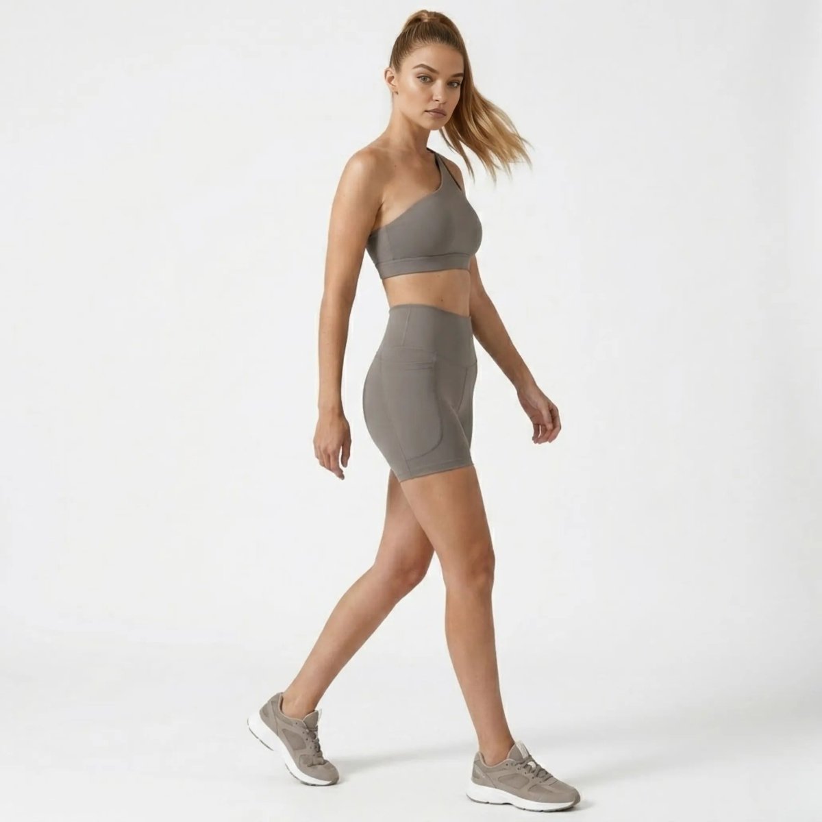 Side profile of model walking in Kouvr grey high waisted workout shorts with side pockets and matching one shoulder top.