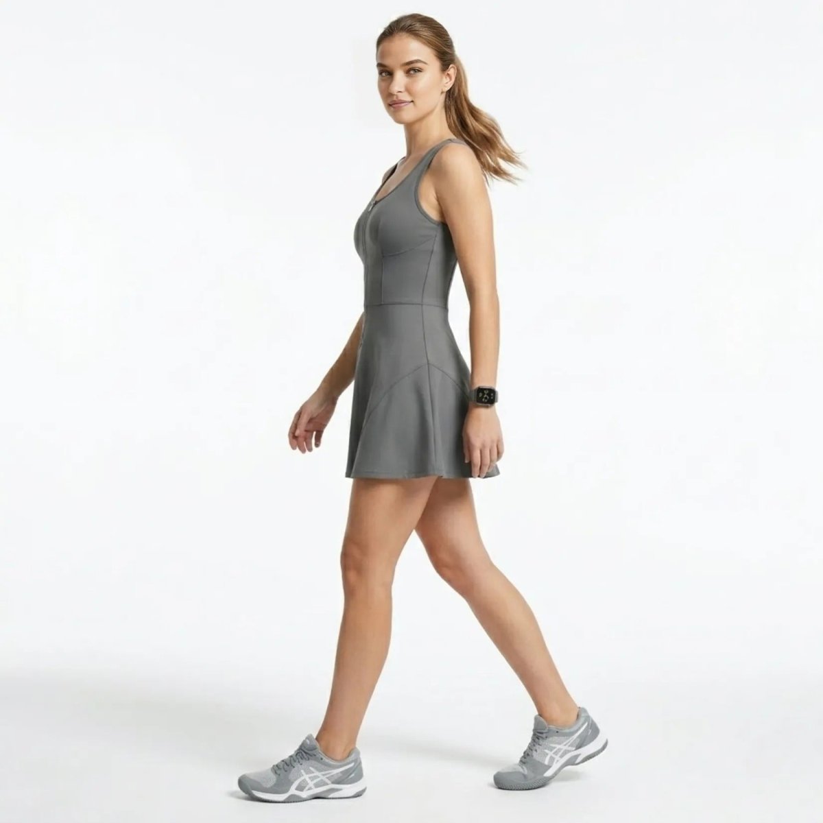 Side profile of a woman walking in a fitted grey activewear racerback mini dress with half zip front