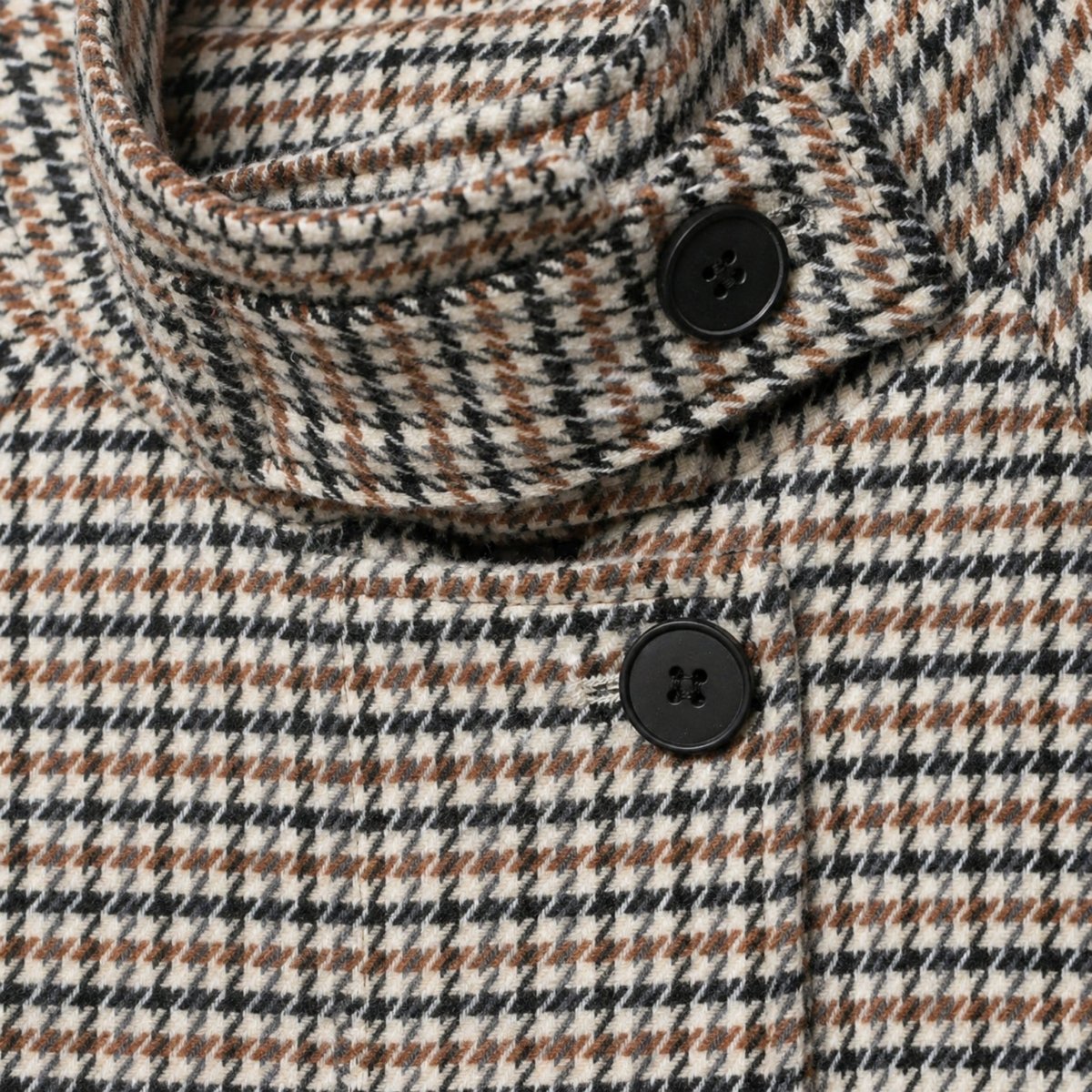 Close-up detail of the high stand collar on a houndstooth jacket showing the black button closure and woven plaid fabric texture.