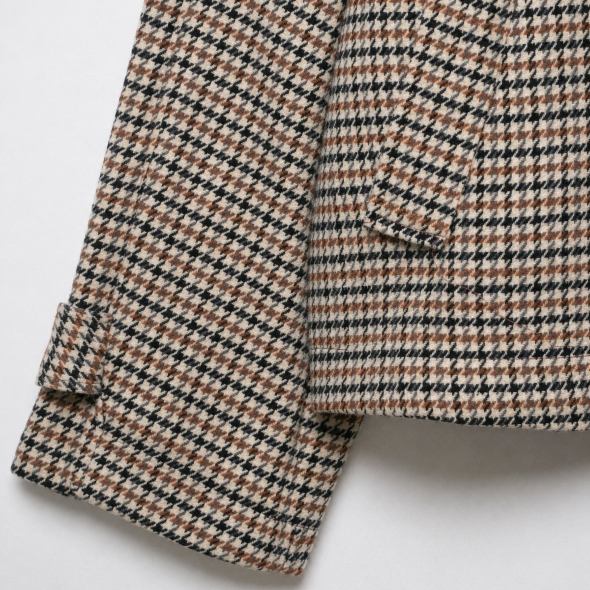 Close-up of the sleeve cuff on a women's houndstooth jacket highlighting the button tab detail and premium wool blend pattern.