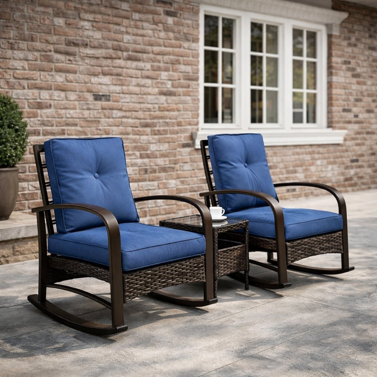 Kouvr 3-piece outdoor wicker rocking chair set with navy blue tufted cushions and glass side table styled on a classic brick patio.