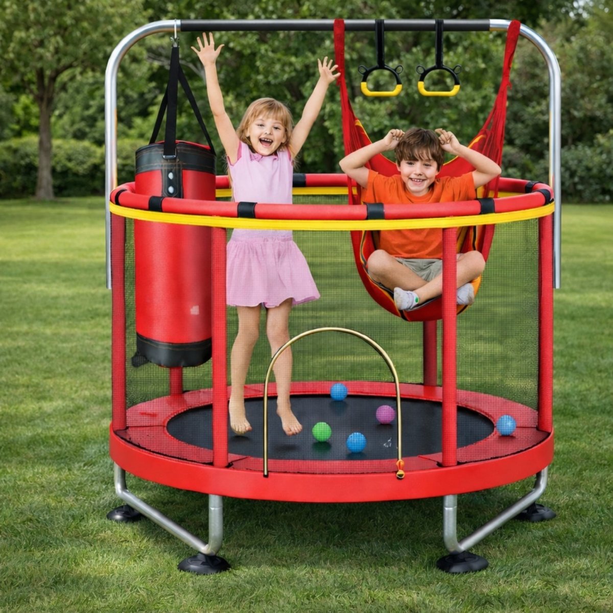 Young girl jumping happily on a red Kouvr 4-in-1 mini trampoline with a safety net, while a boy sits smiling in the attached red swing seat outdoors on a green lawn.