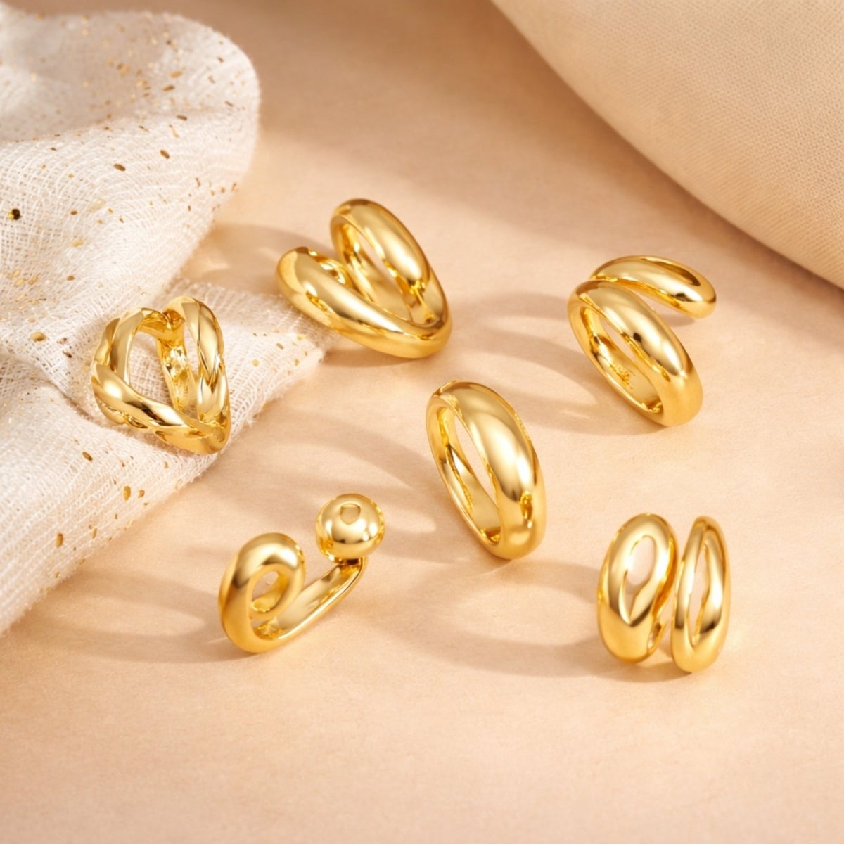 A flatlay product shot of the six unique Kouvr statement gold rings, arranged on a beige surface to display their individual sculptural and modern designs.
