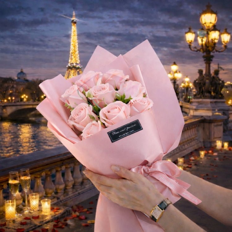 A hand-tied bouquet of 9 light pink forever roses from Kouvr, wrapped in pink paper, held by a woman in a romantic Parisian setting.