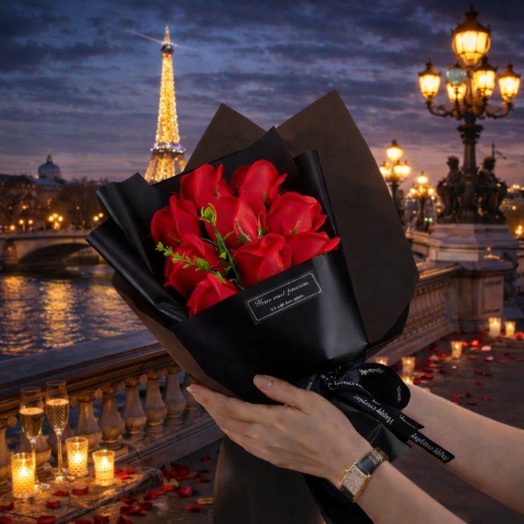 A woman holding a luxury bouquet of 9 red forever roses from Kouvr, wrapped in black paper, with the Eiffel Tower in the background at twilight.