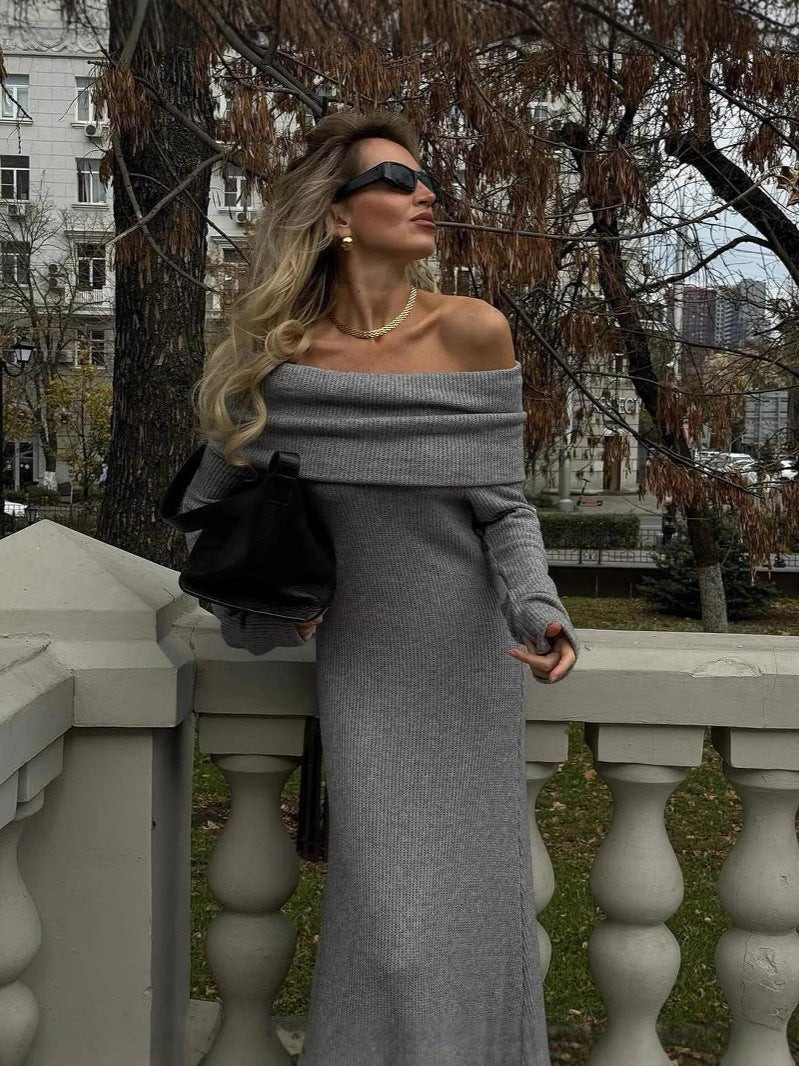 A woman with blonde hair wearing the Kouvr Ingrid grey off-the-shoulder knit maxi dress, viewed from the side while standing on a balcony.