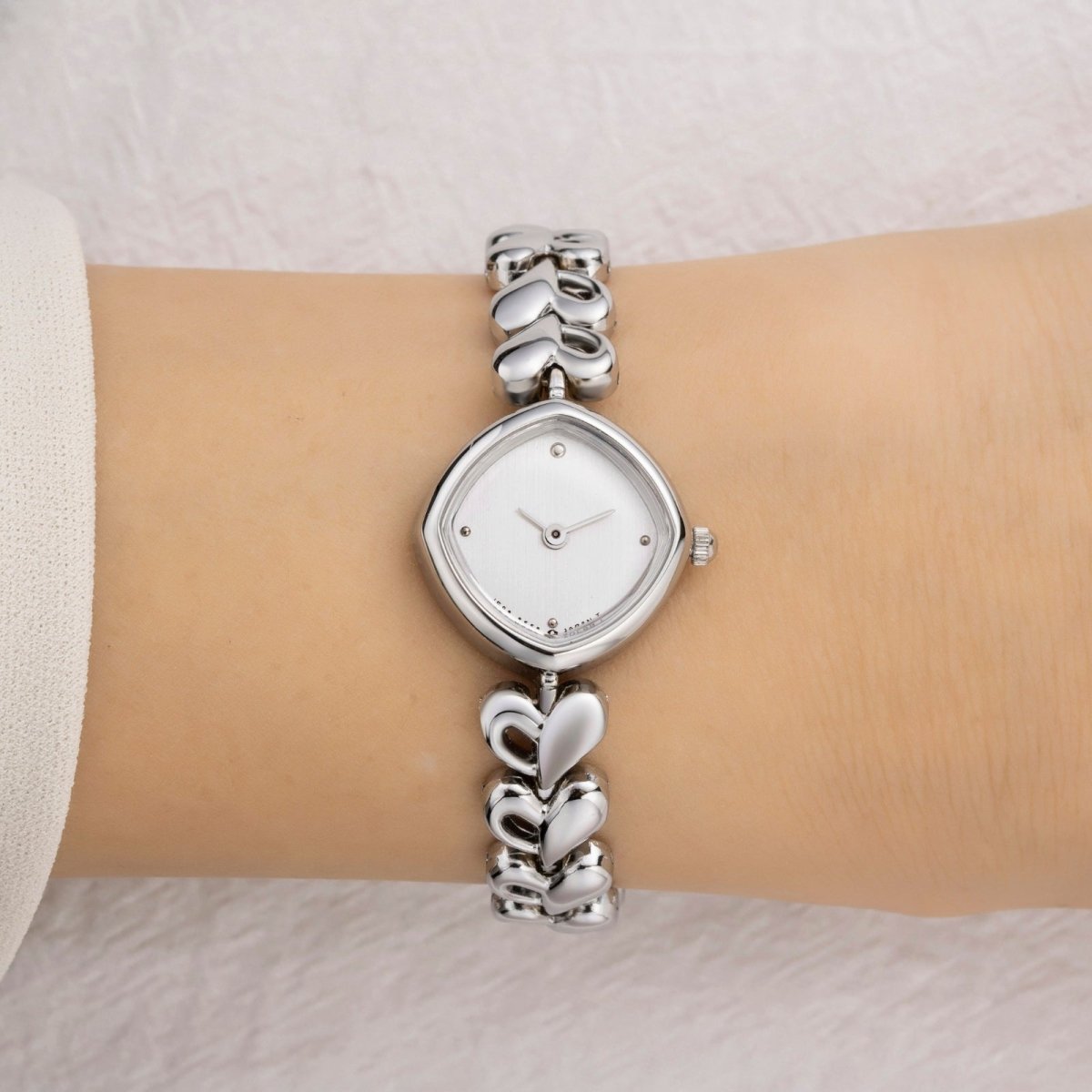 Silver kouvr wristwatch with heart designs on a wrist against a neutral background