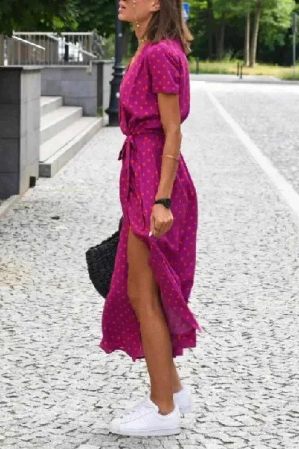 Woman walking in the Kouvr Aleia magenta and orange polka dot midi wrap dress with white sneakers