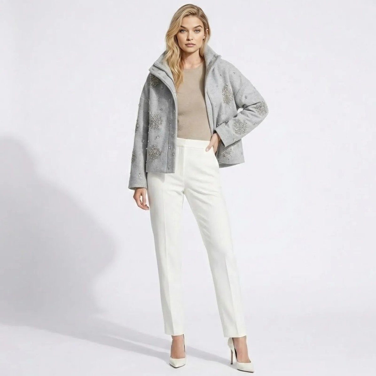 Model wearing the Kouvr Alisa light grey wool-blend jacket with crystal snowflake embellishments, styled with a beige top, white trousers, and white heels, against a white studio background.