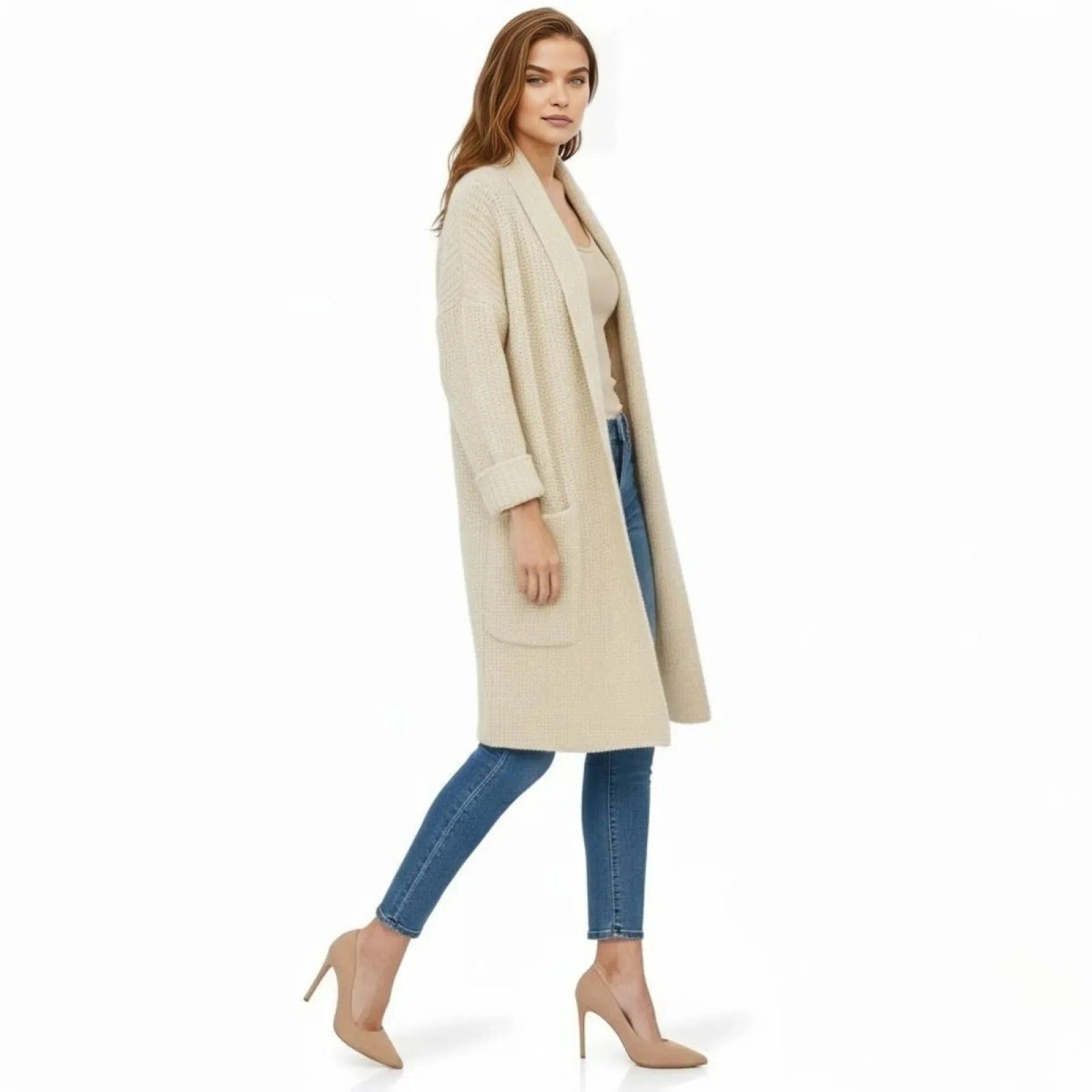 Side profile of a woman walking in a ivory longline waffle knit cardigan with pockets, paired with denim and heels.