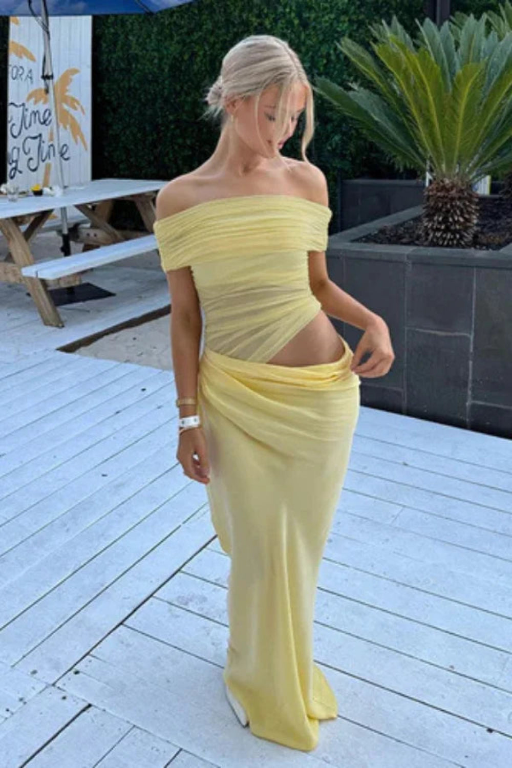 Model wearing the Kouvr Anita Gown in Lemon Chiffon, a yellow off-the-shoulder maxi dress with a side waist cutout