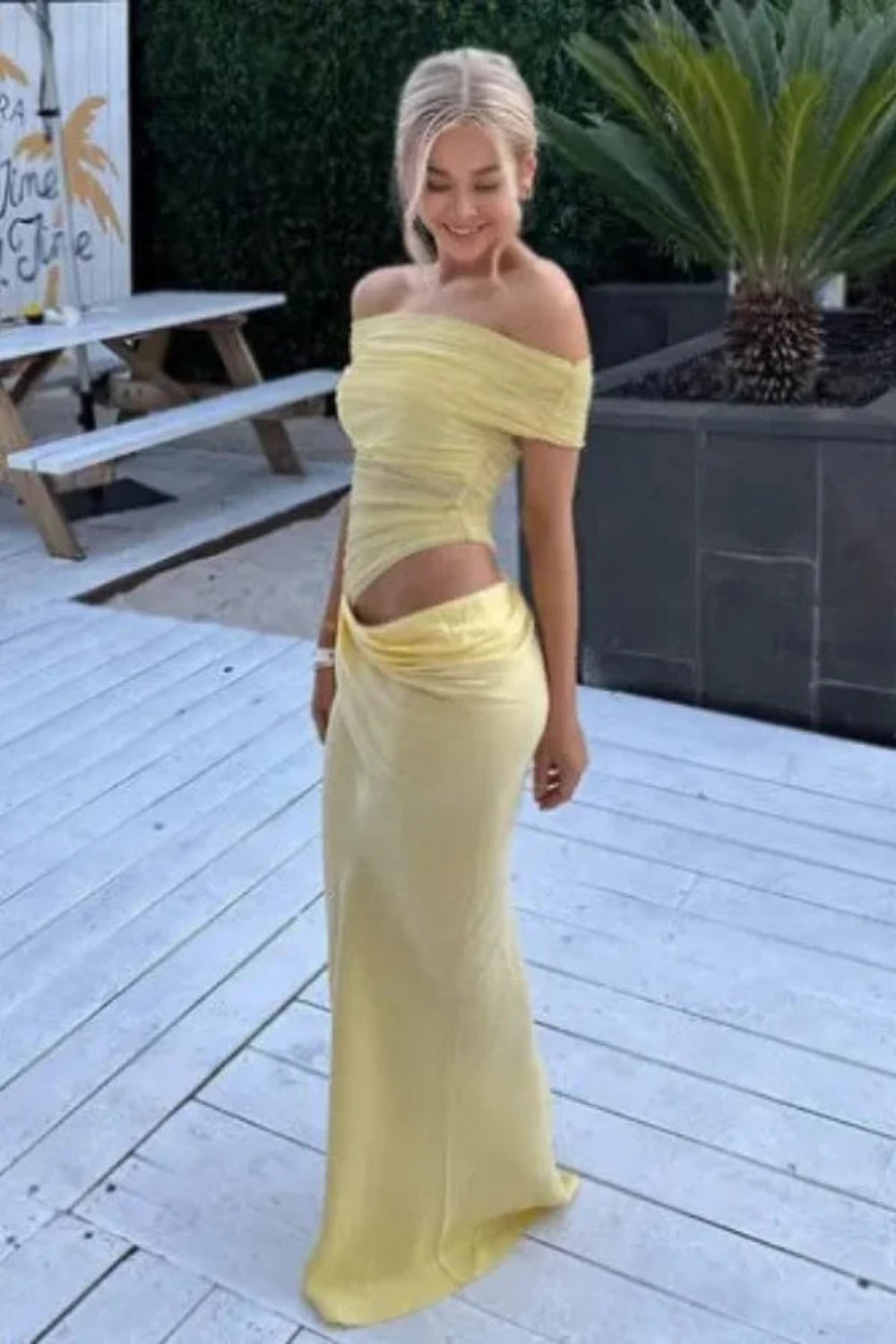 Model wearing the Kouvr Anita Gown in Lemon Chiffon, a yellow off-the-shoulder maxi dress with a side waist cutout