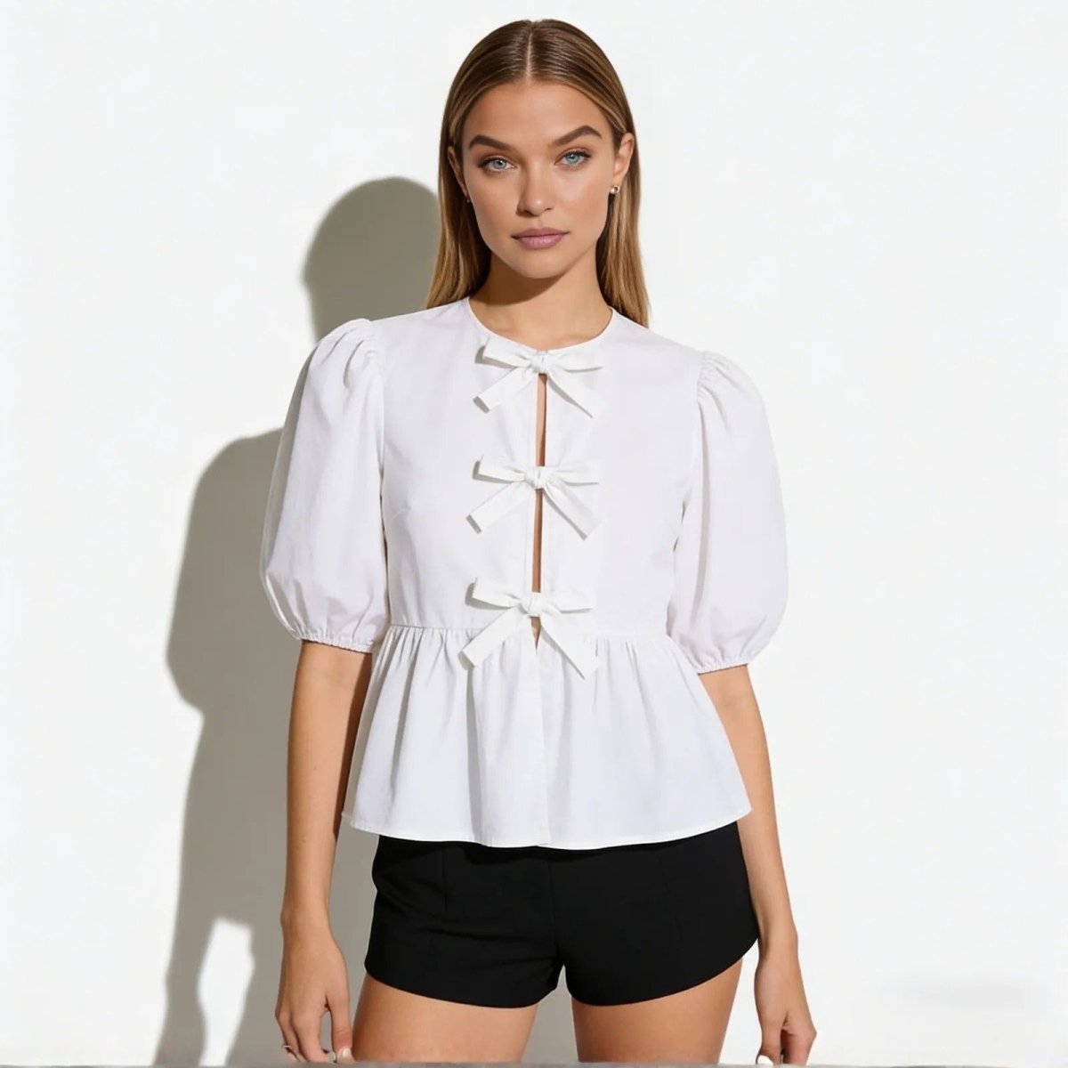Model wearing the Kouvr Anne white cotton poplin blouse with puff sleeves and three front bows, paired with black shorts.