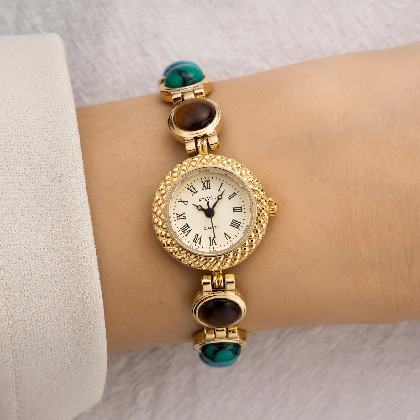 Gold kouvr wristwatch with gemstone accents on a wrist against a neutral background