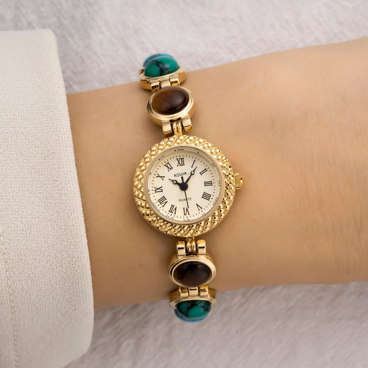 Gold kouvr wristwatch with gemstone accents on a wrist against a neutral background
