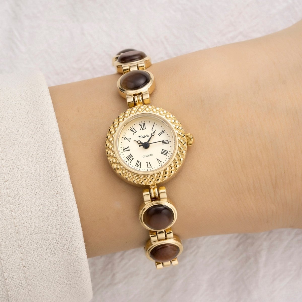 Gold kouvr wristwatch with brown gemstones on a wrist against a white background