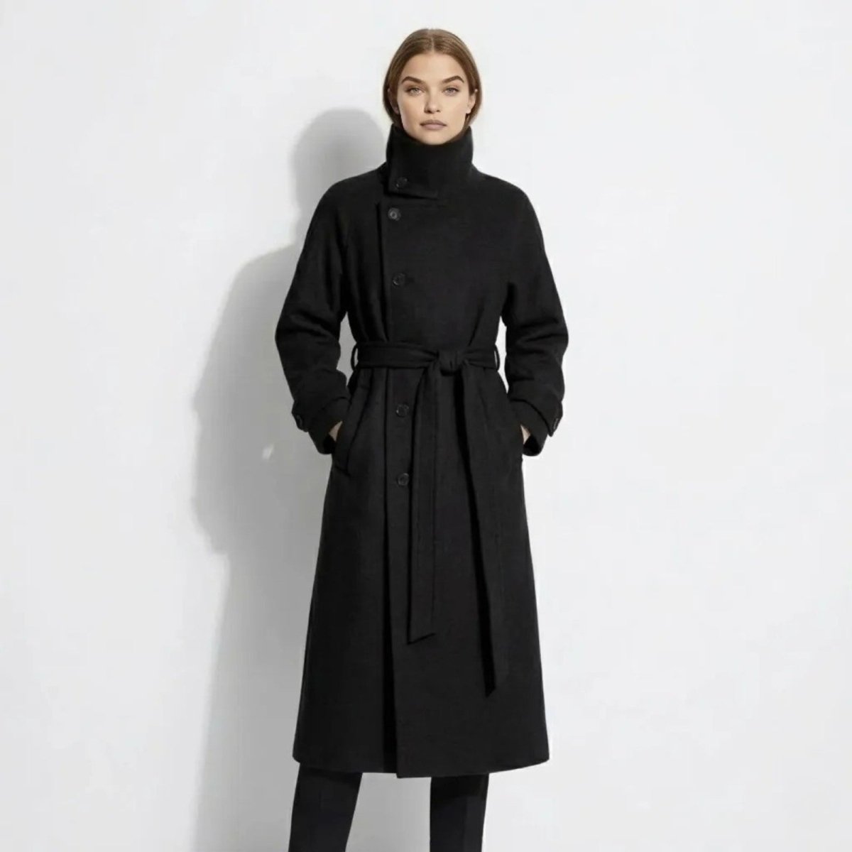 Model wearing the Kouvr Ashley long black belted wool coat with a high funnel neck, viewed from the front.
