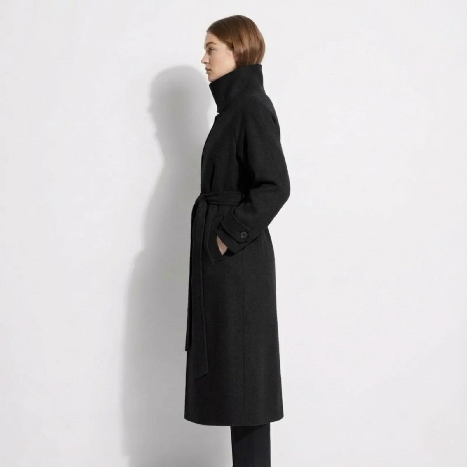 Side profile of the Kouvr Ashley long black wool wrap coat showing its length and silhouette on a model.