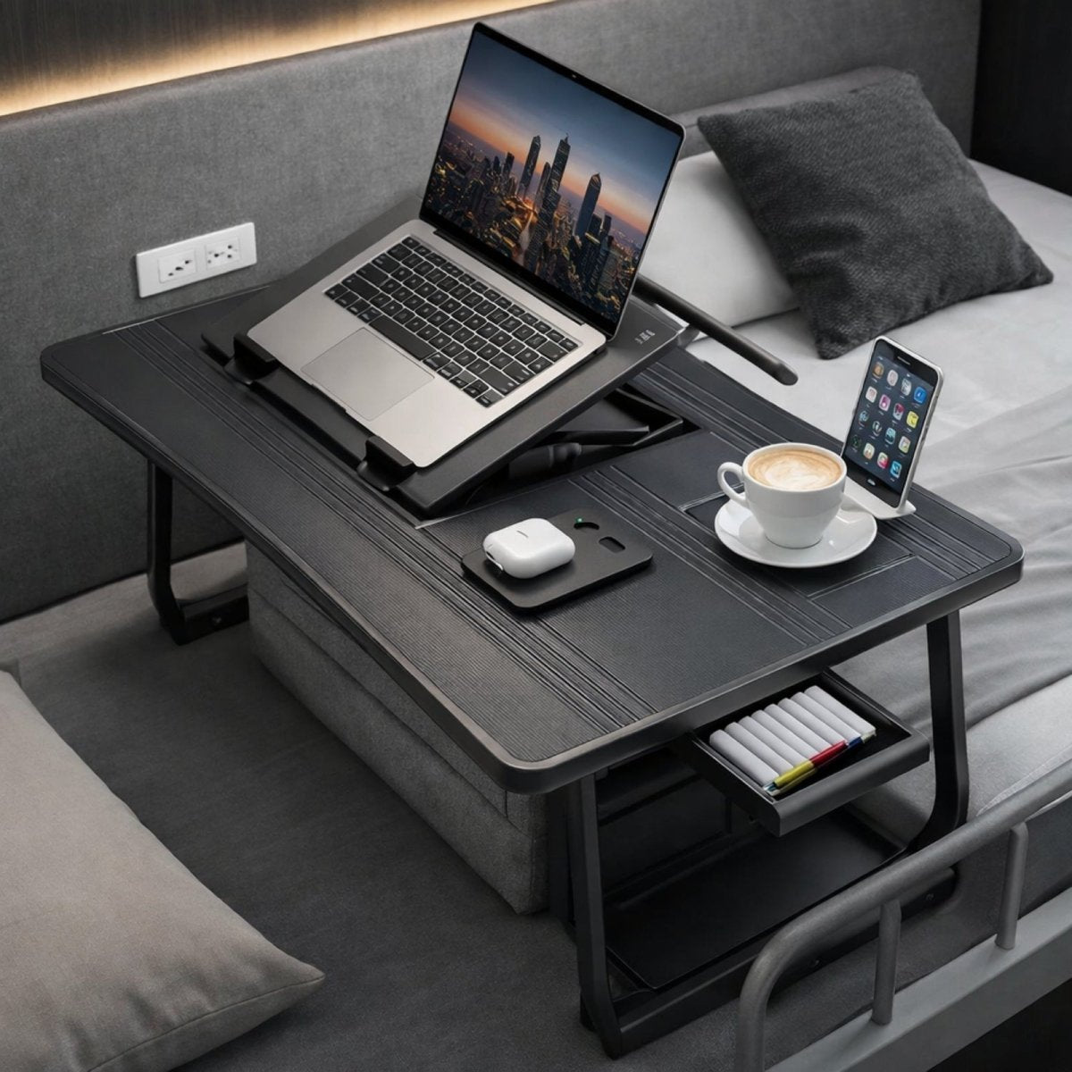 Sleek black edition of the Kouvr bed desk shown with an open side drawer holding pens, emphasizing the modern aesthetic and organizational storage features.